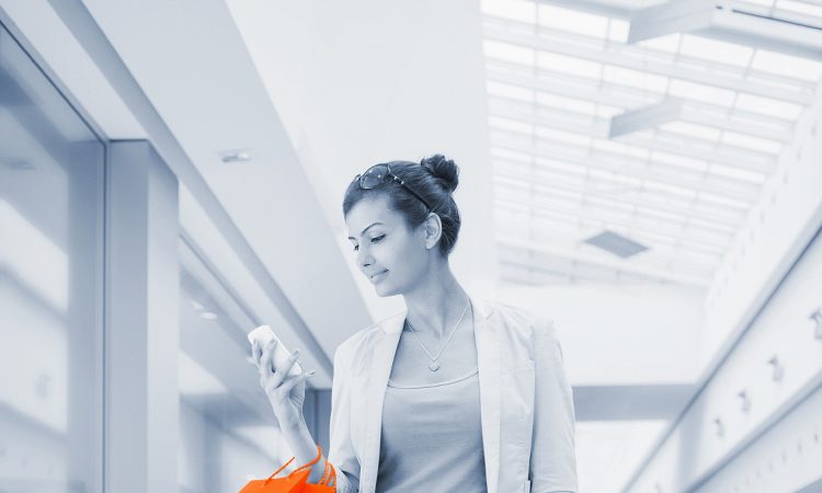 Młoda kobieta w galerii handlowej trzymająca torby z zakupami i smartfona