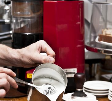 Barista w kawiarni nalewa spienione mleko do kubków cappucino