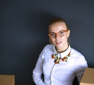 Młoda kobieta w białej bluzce i okularach siedzi przed laptopem