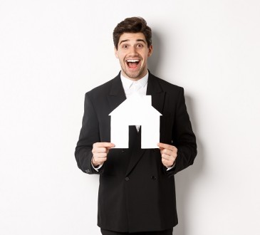 Roześmiany mężczyzna w garniturze trzyma szablon w kształcie domu