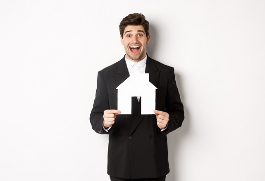 Roześmiany mężczyzna w garniturze trzyma szablon w kształcie domu